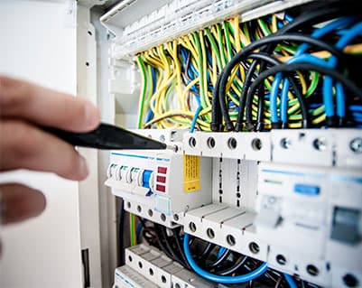 Técnico realizando mantenimiento en un cuadro eléctrico industrial, con destornillador en mano y cableado multicolor organizado en riel DIN.