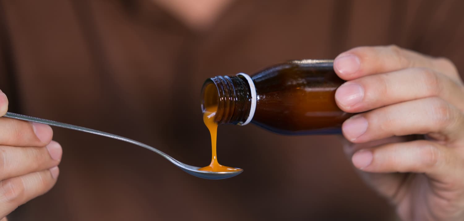 Hombre mano vertiendo medicamentos o jarabe antipirético de botella a cuchara
