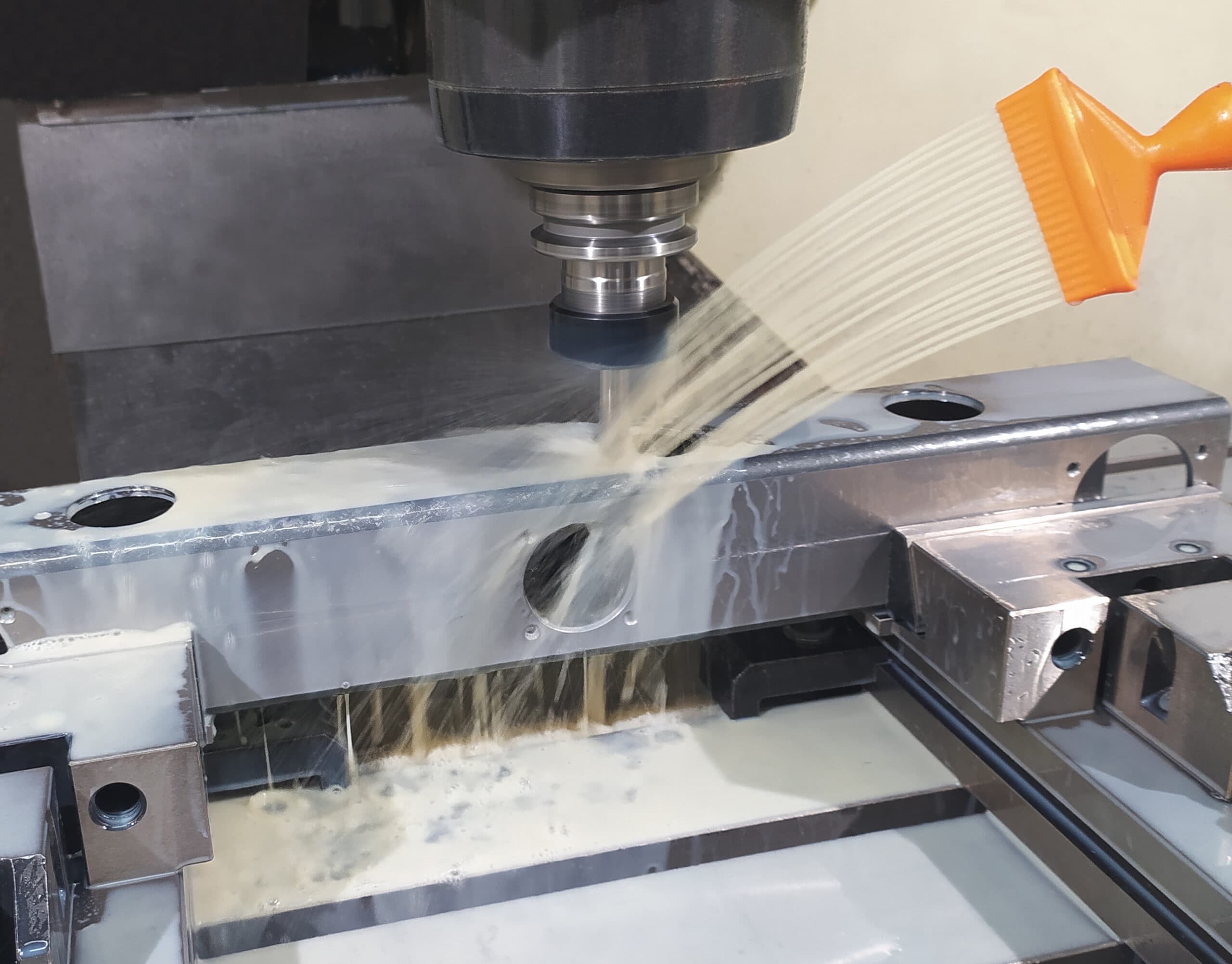 Proceso de mecanizado CNC con refrigerante líquido a presión sobre una pieza de aluminio en una fresadora de control numérico.